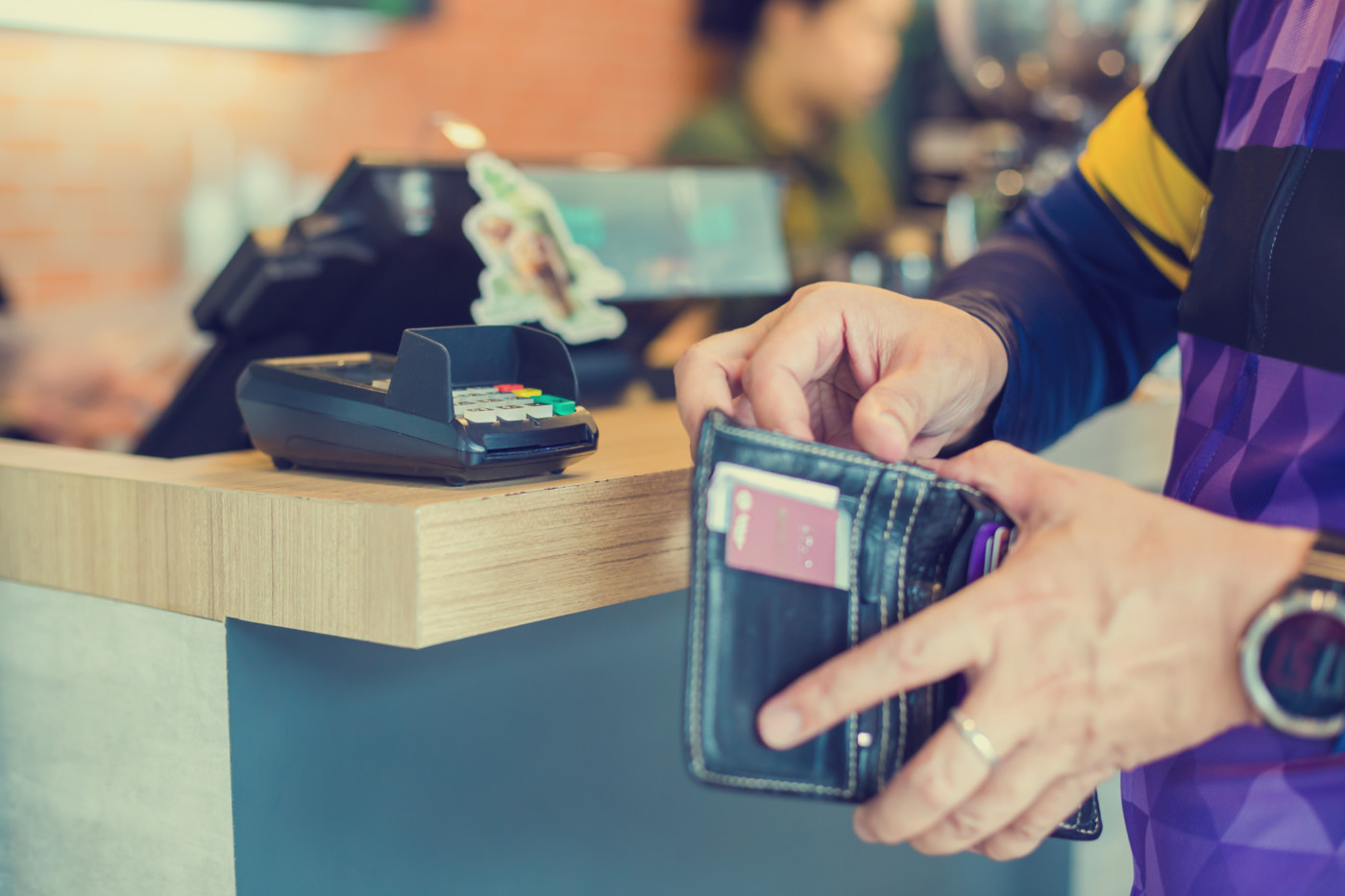 Selective focus to credit card reader with blurry the man picking up banknotes or credit card in the wallet to pay at the counter service. Self service payment in modern shop, Self-service pay point.